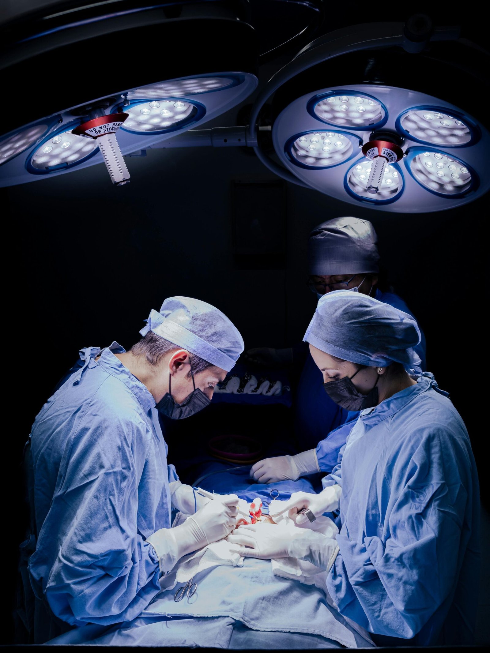 Team of surgeons performing an operation under bright surgical lights in a hospital.